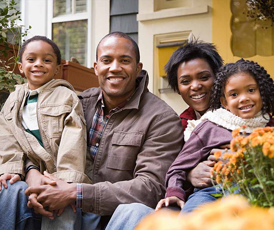 A smiling family of four sitting together outside their home.